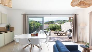 A modern kitchen with white cabinets and a dining area with a white table and chairs. There is a blue sofa and a wicker hanging light fixture.
