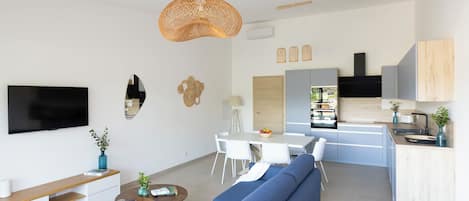 Una sala de estar moderna con un sofá azul, una mesa de comedor y una zona de cocina con armarios grises.