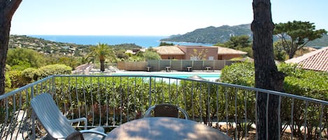 A terrace with a table and chairs, overlooking a swimming pool and a coastal view.