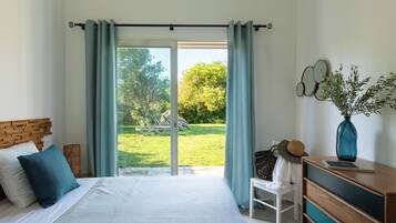 A bedroom with a bed, a chair, a dresser, and a view of a garden through a sliding door.