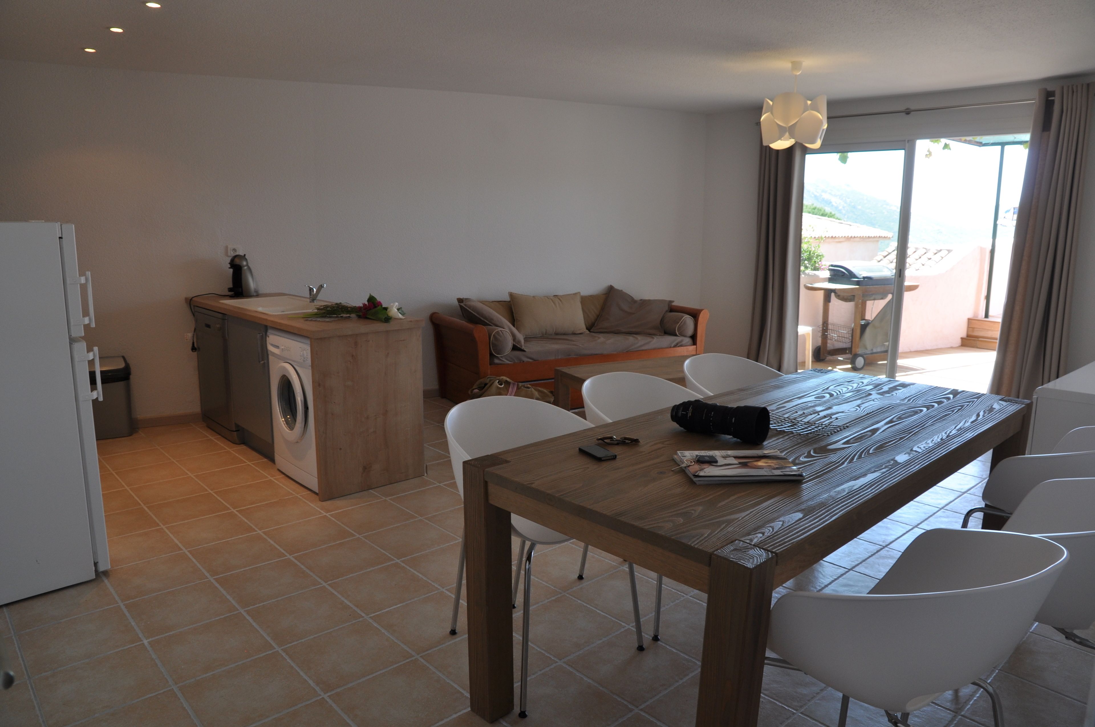 A compact living space with a kitchenette, a dining table with chairs, a sofa, and a sliding glass door leading to an outdoor area.