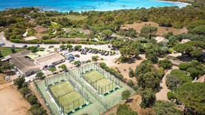 Vista aérea de una zona costera con un complejo de canchas de tenis, un estacionamiento y una playa.