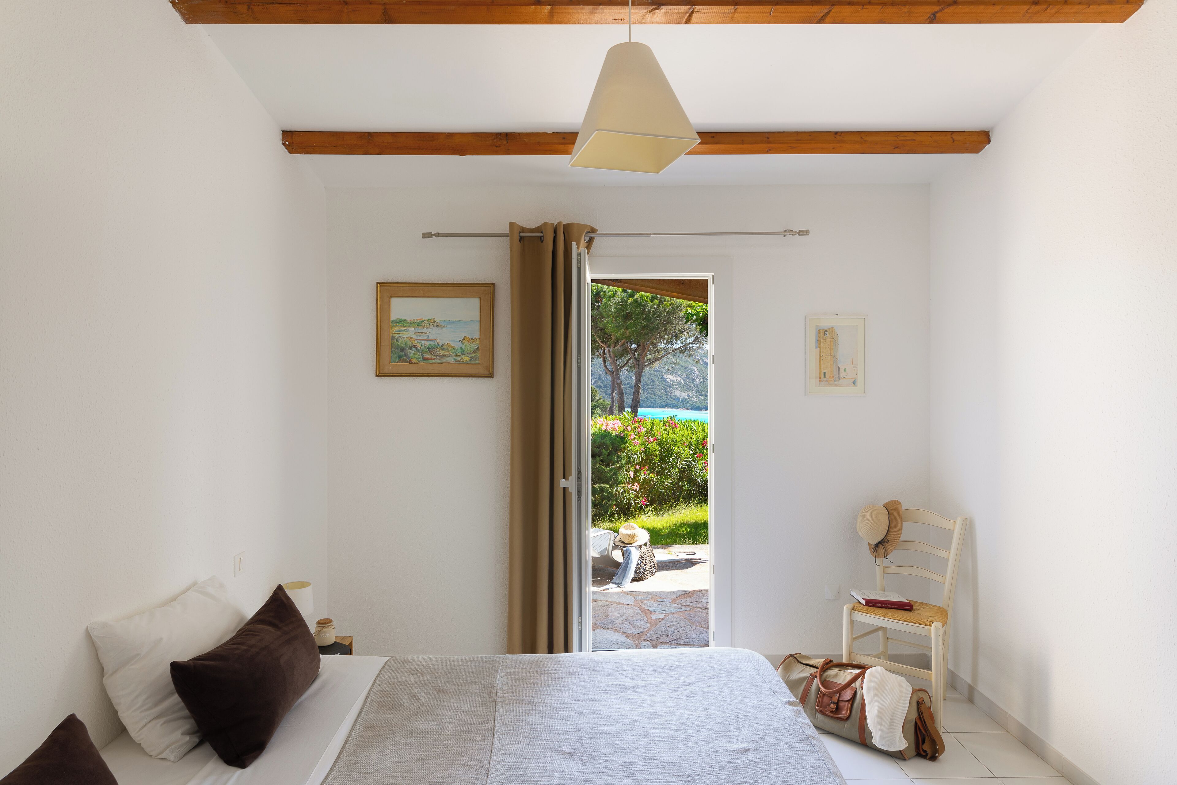 Un dormitorio con una cama, una silla, una maleta y vistas al exterior.
