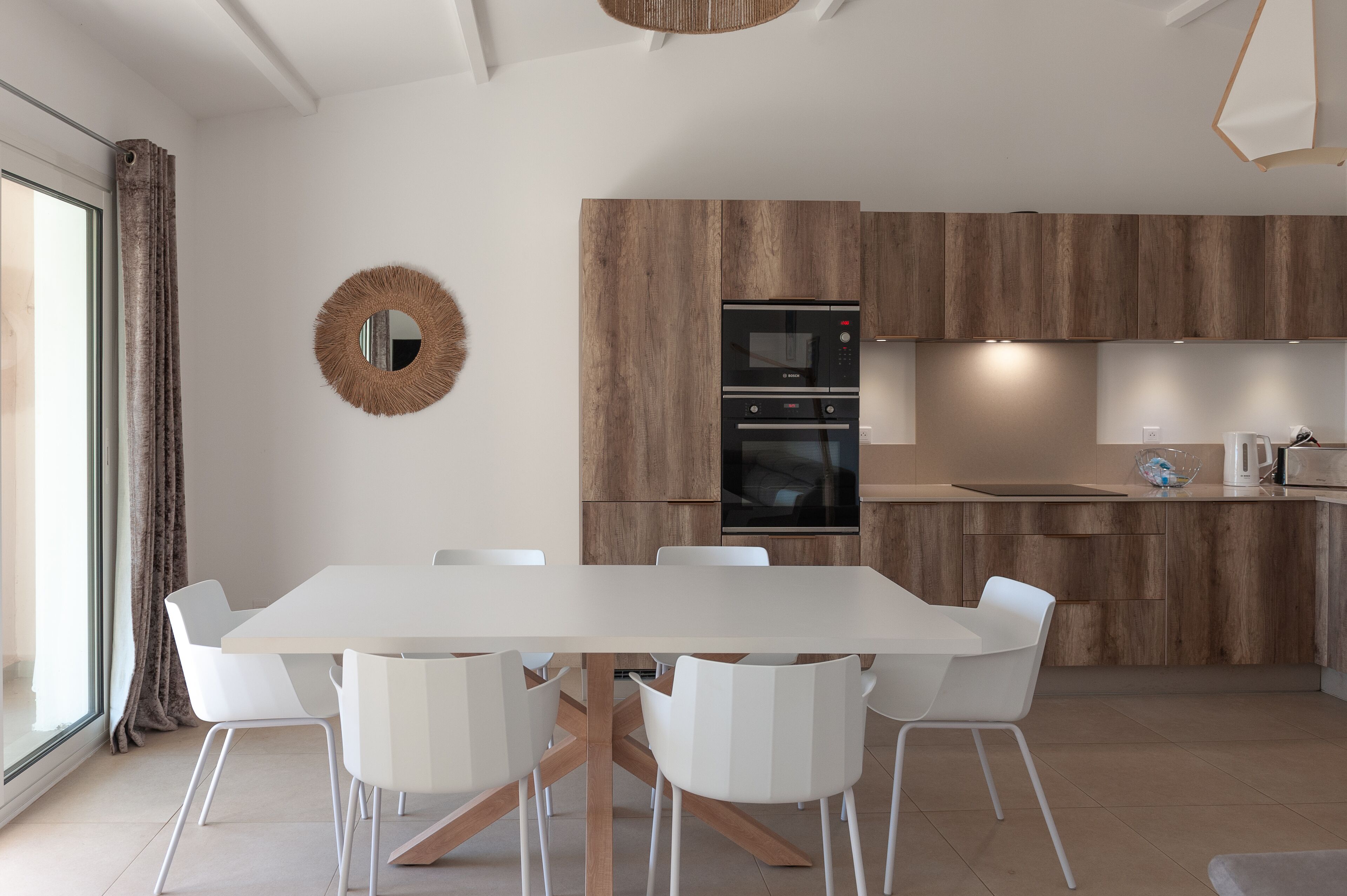 A modern kitchen with wooden cabinets, a built-in oven, and a dining area with a white table and chairs.