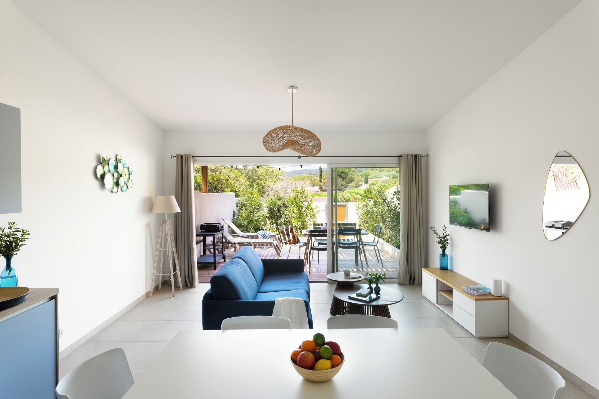 A modern living room with a sofa, dining table, and a view of the garden through the glass door.