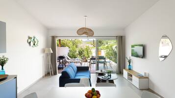 Un salon moderne avec un canapé, une table à manger et une vue sur le jardin, visible à travers la porte vitrée.