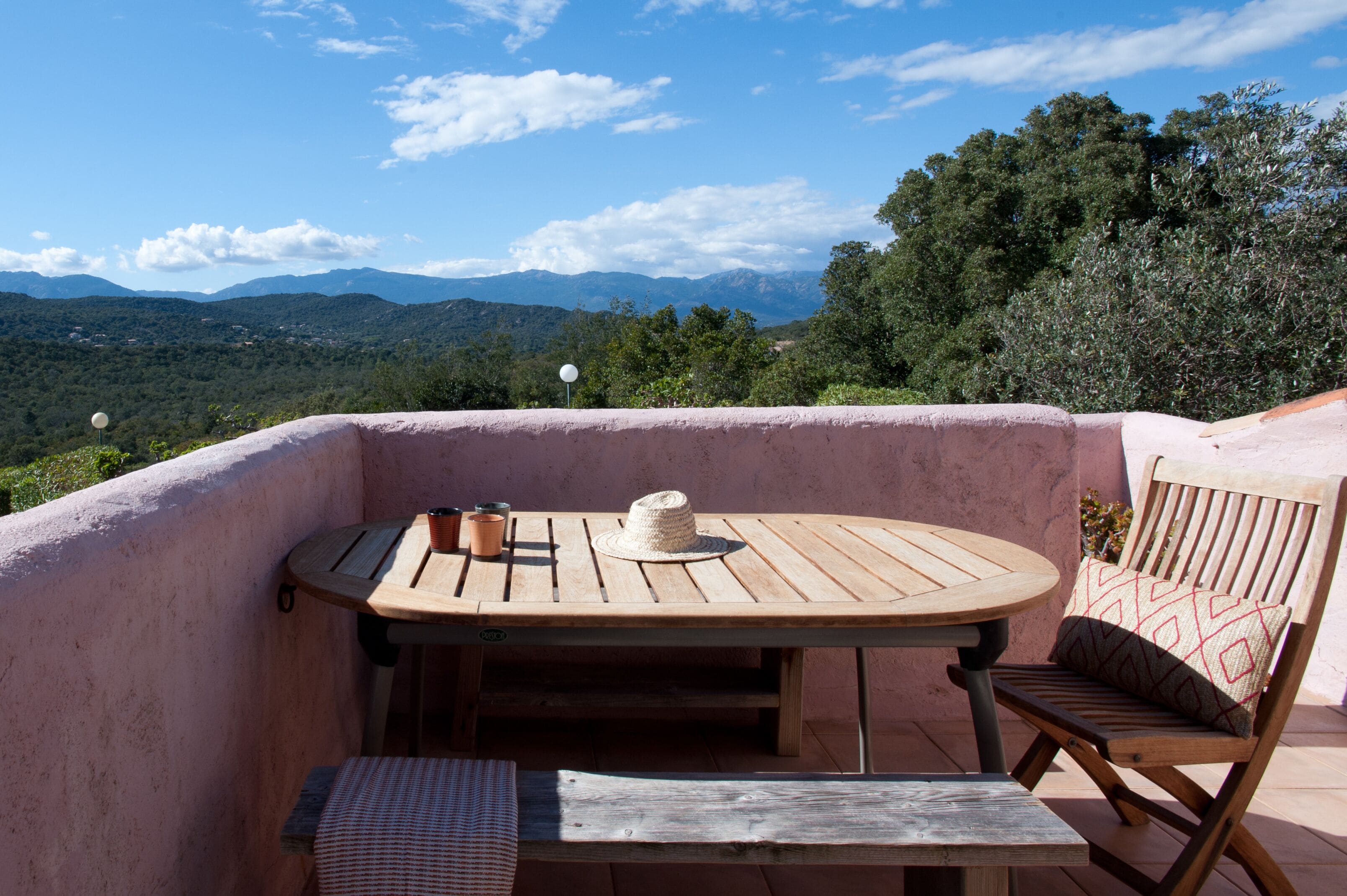 A wooden table and chair set on a balcony with a view of mountains and trees.