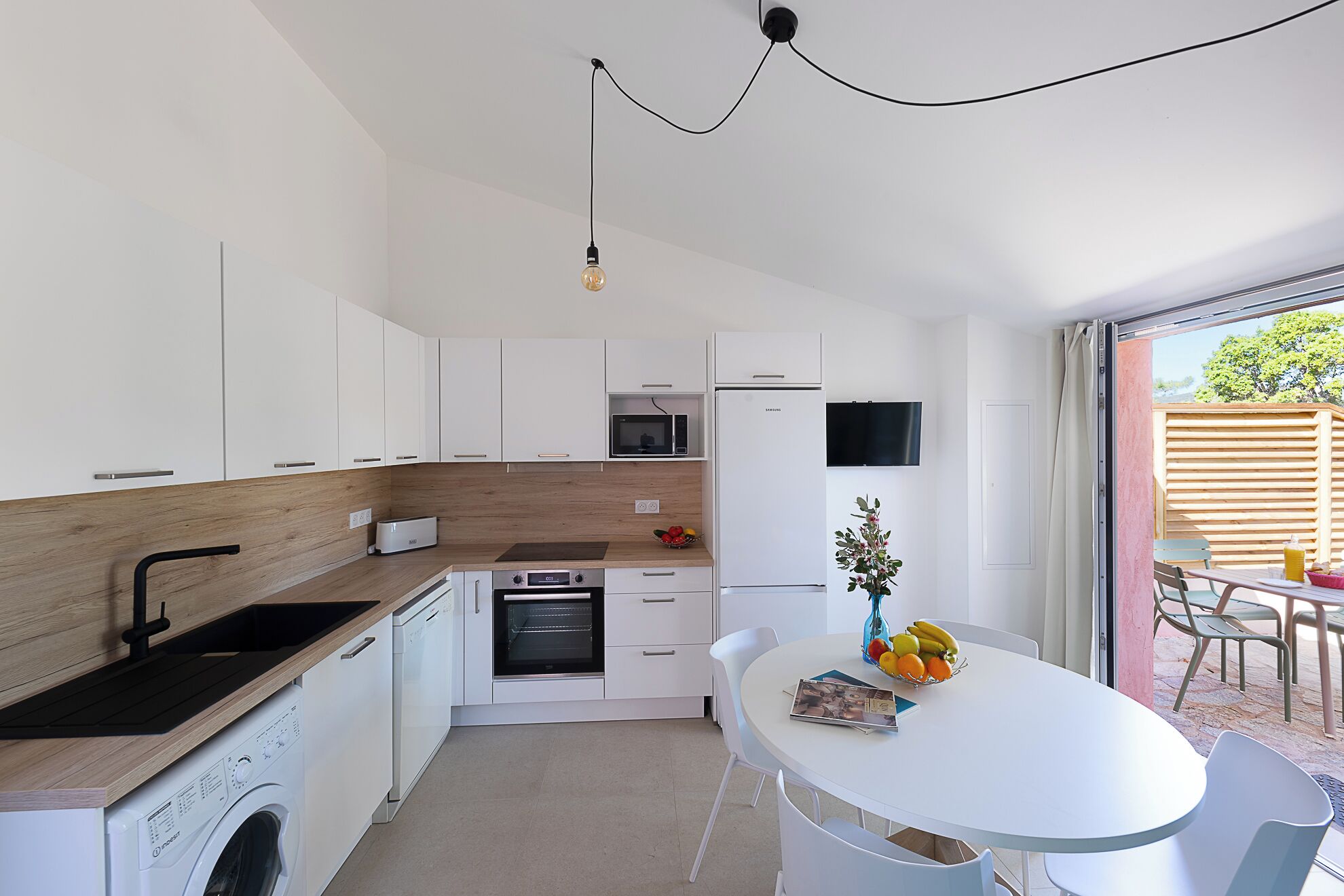 A modern kitchen with white cabinets, a wooden countertop, a built-in oven, and a dining area with a white table and chairs.