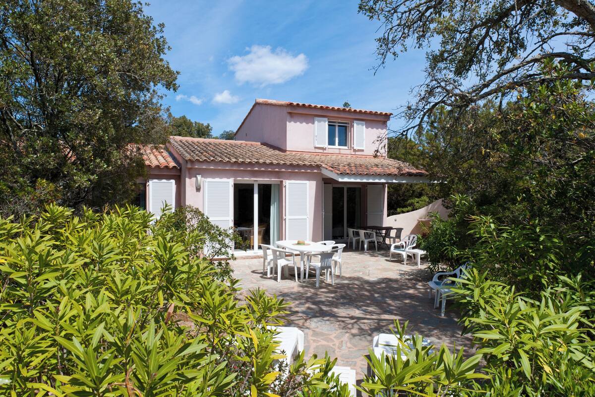 A two-story house with a tiled roof, a patio with outdoor furniture, and a garden with various plants.