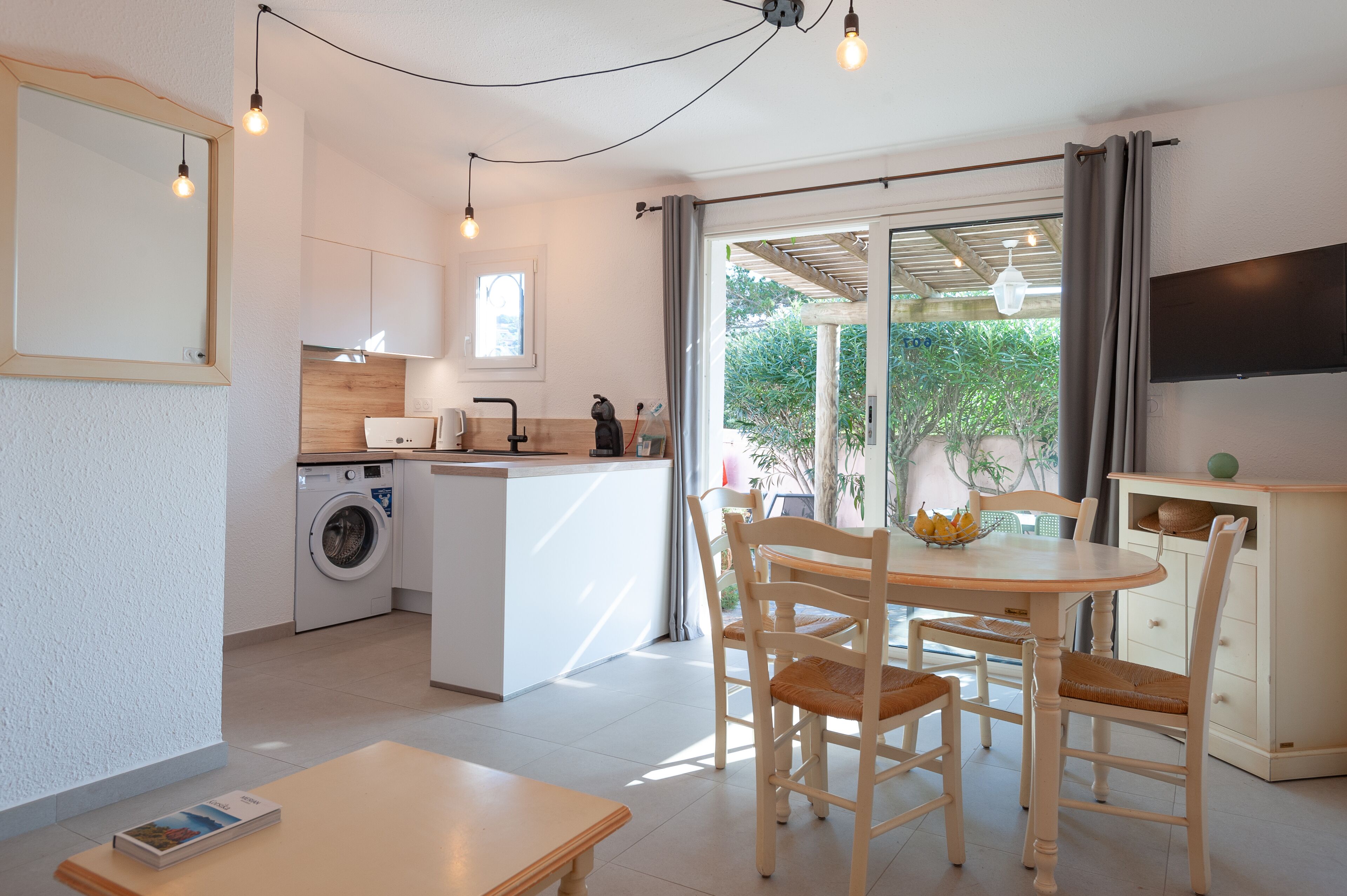A compact kitchen with a washing machine, a dining area with a table and chairs, and a large sliding glass door leading to an outdoor area.