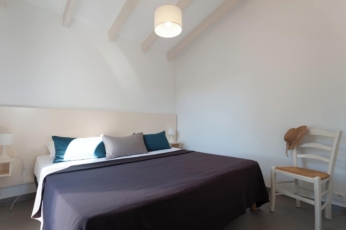 A bedroom with a bed, a chair, a nightstand, and a lamp.