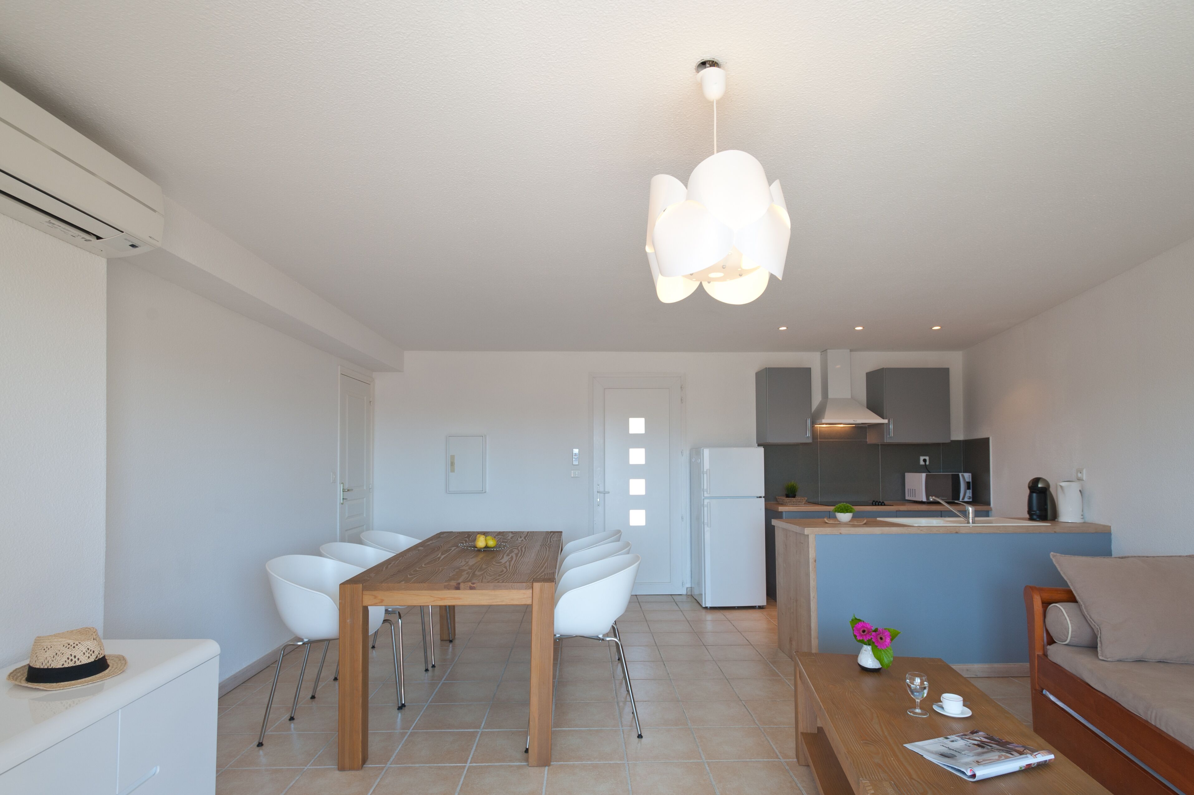 Eine moderne Küche mit weißen Geräten, ein Essbereich mit einem Holztisch und weißen Stühlen sowie ein Wohnbereich mit Sofa und Couchtisch.