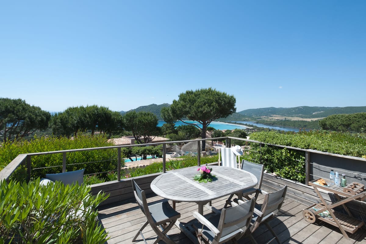 A wooden deck with a table and chairs, overlooking a pool and scenic landscape.