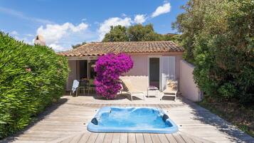 A wooden deck with a hot tub, a pink house, and a purple flowering bush.