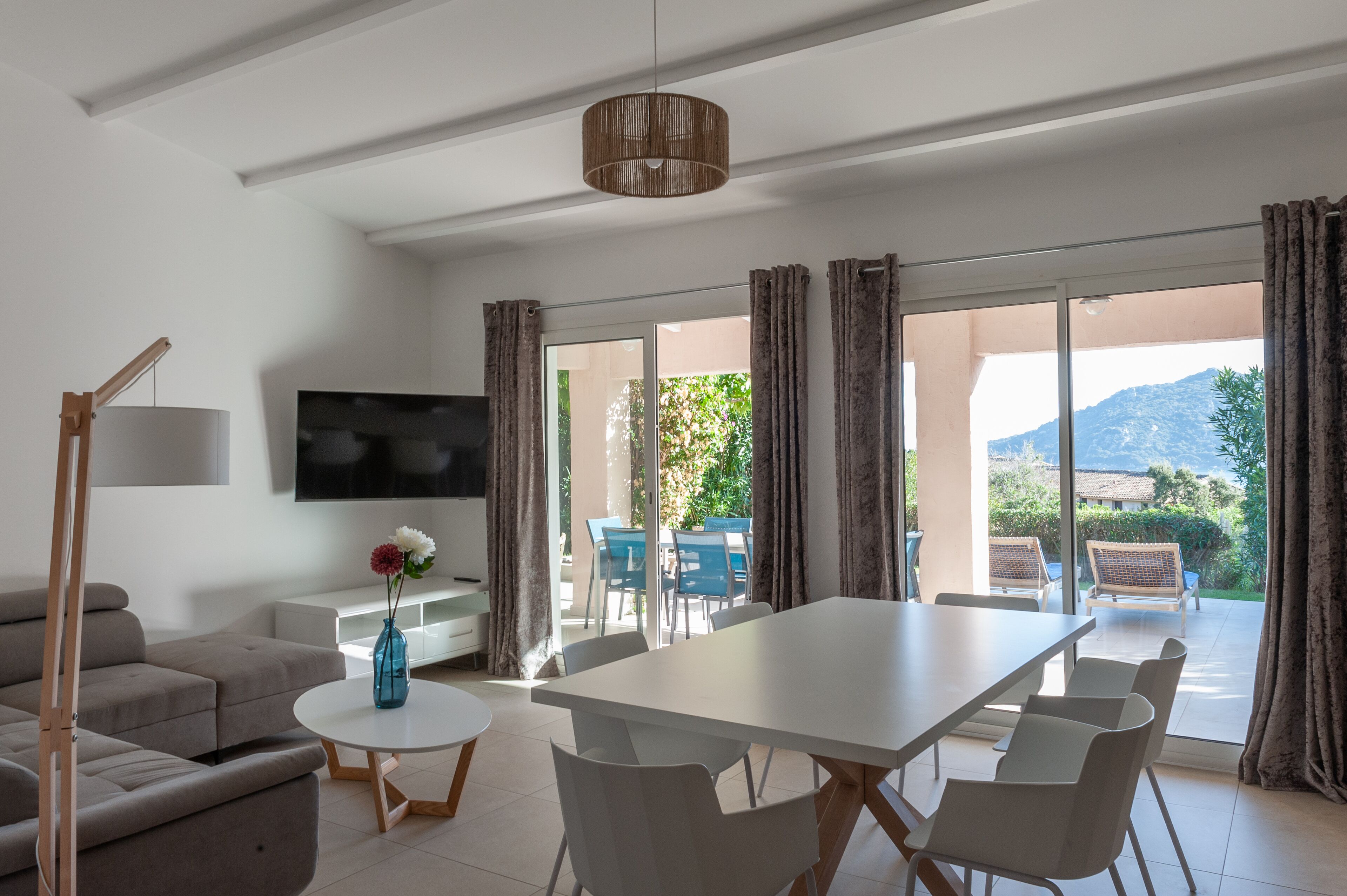 Una sala moderna con un sofá blanco, una mesa de centro redonda, un televisor de pantalla plana y un comedor con una mesa y sillas blancas.