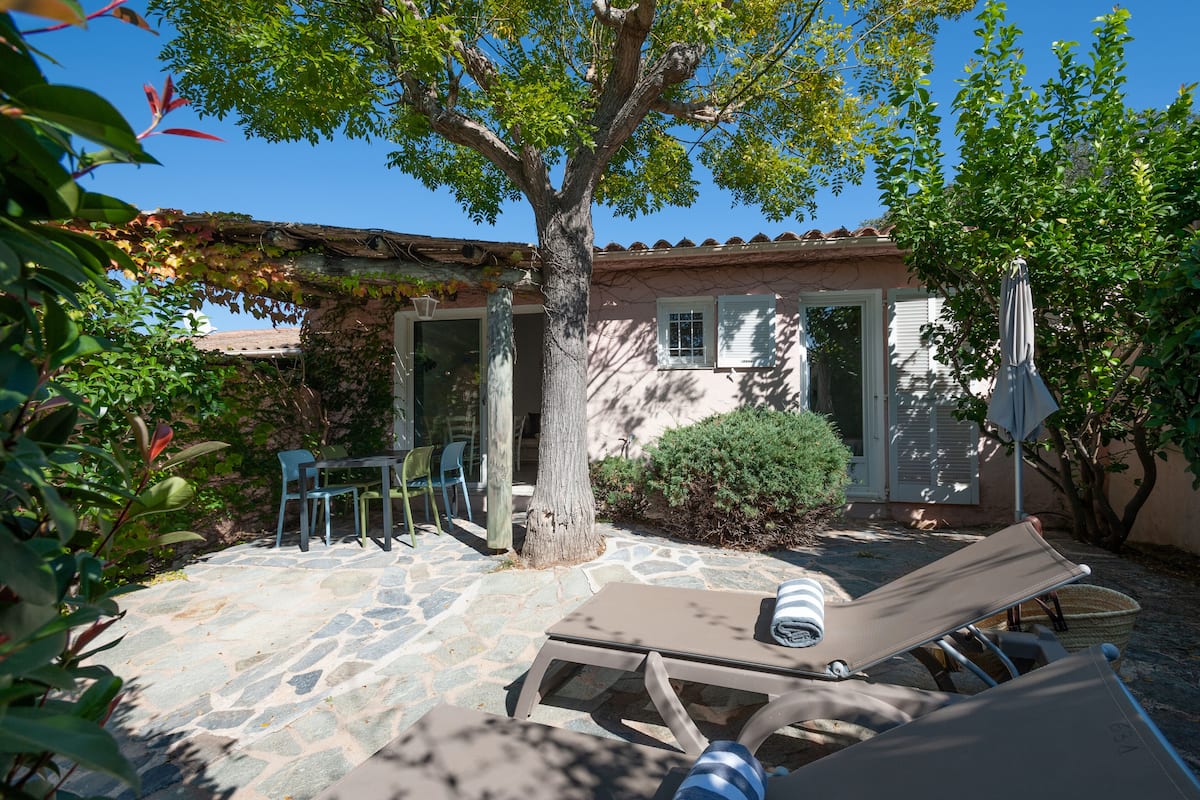A stone patio with a tree, outdoor furniture, and a building with a tiled roof.
