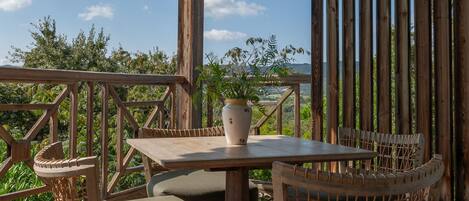 A wooden deck with a table and chairs, a potted plant, and a view of the landscape.