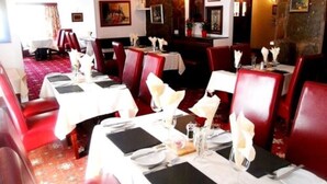 Restaurante com cadeiras estofadas vermelhas e toalhas de mesa brancas. Mesas montadas com pratos, copos e talheres.
