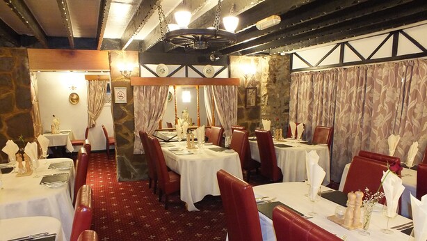 Restaurante com mesas redondas, cadeiras estofadas vermelhas e um tapete estampado.