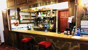 Uma área de bar com banquetas, balcão e diversos tipos de garrafas.