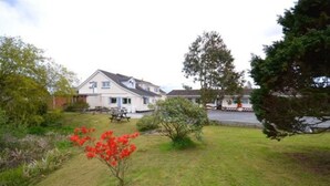 Uma casa residencial com gramado, mesa para piquenique e um pequeno jardim com flores vermelhas.