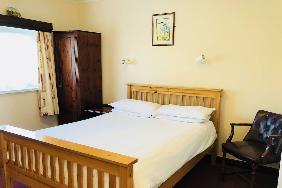Ein Schlafzimmer mit einem hölzernen Bett, einem Sessel, einem Kleiderschrank und einem Bild an der Wand.