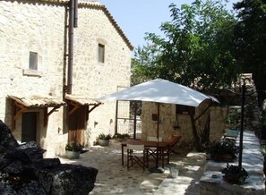 A stone building with a patio area featuring a table and chairs, surrounded by potted plants and a large umbrella. - Country House Case Catalano (Abbateggio)