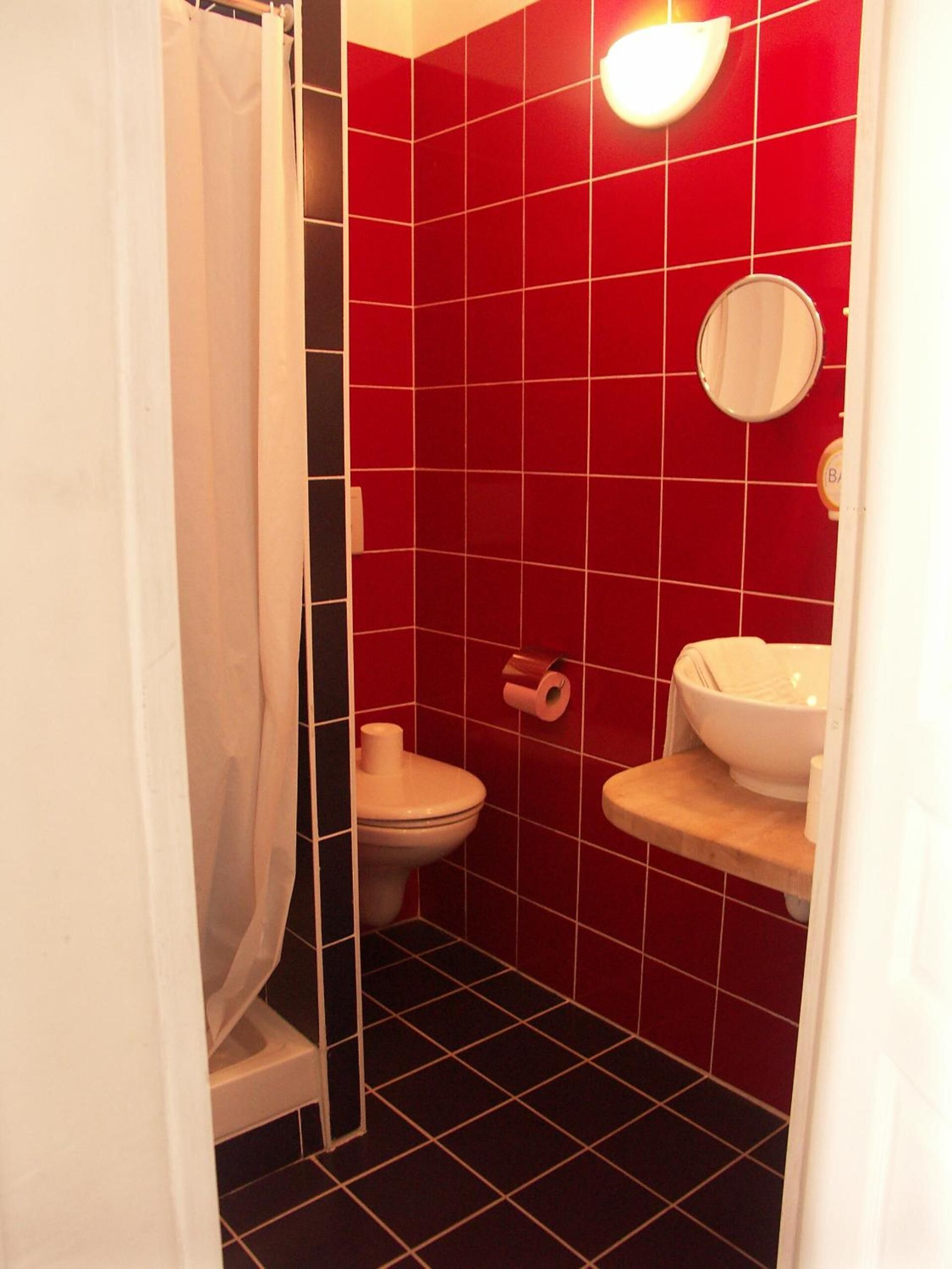 A bathroom with red tiles, a toilet, a sink, and a mirror.