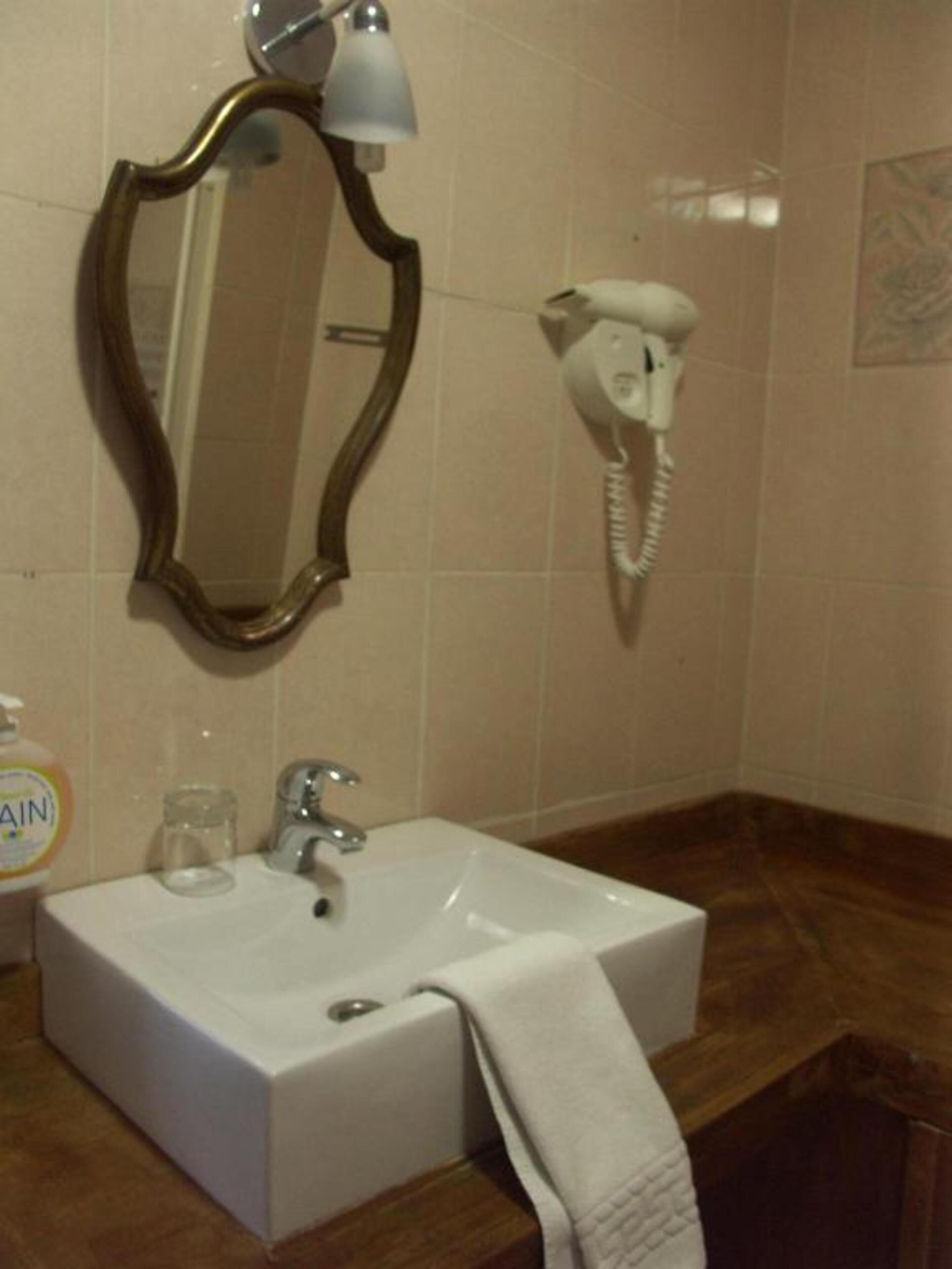 Un baño con un lavamanos blanco, un espejo, un secador de pelo y una botella de jabón para manos.