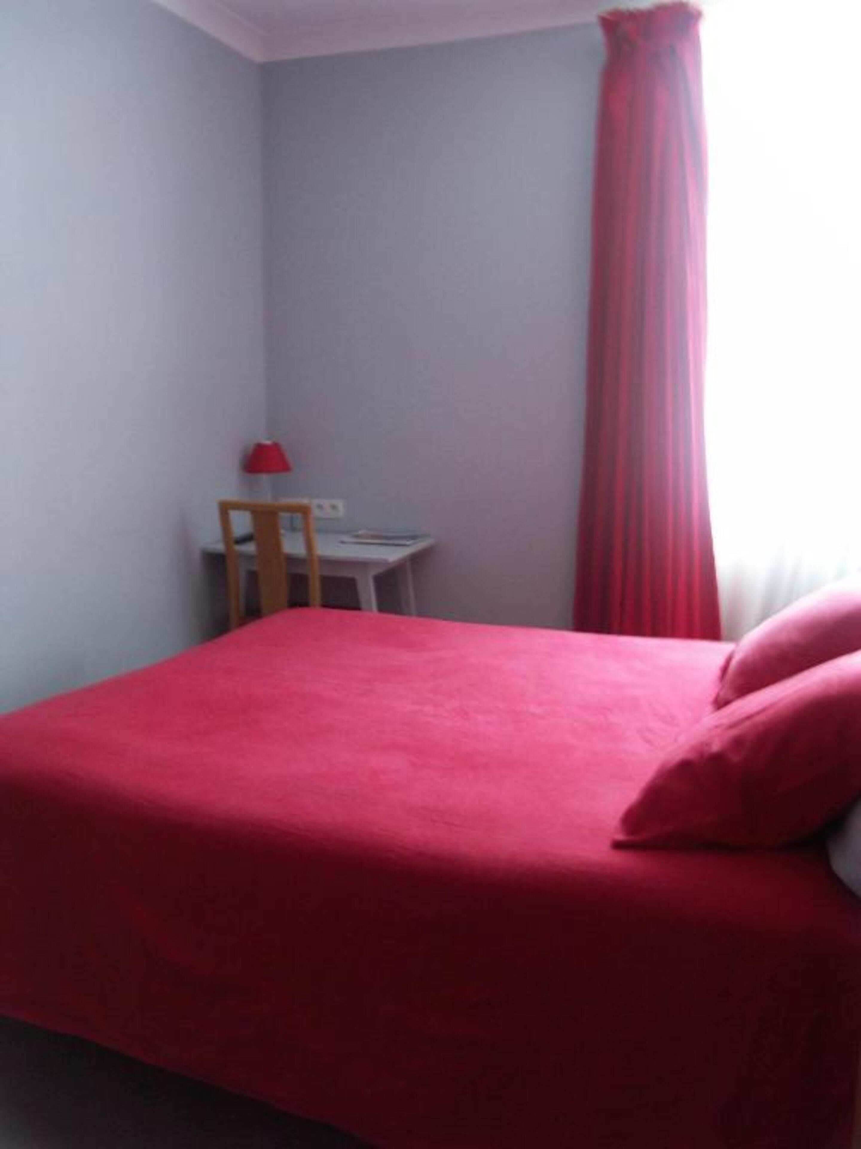 A bedroom with a bed, a chair, a desk, and a window with curtains.