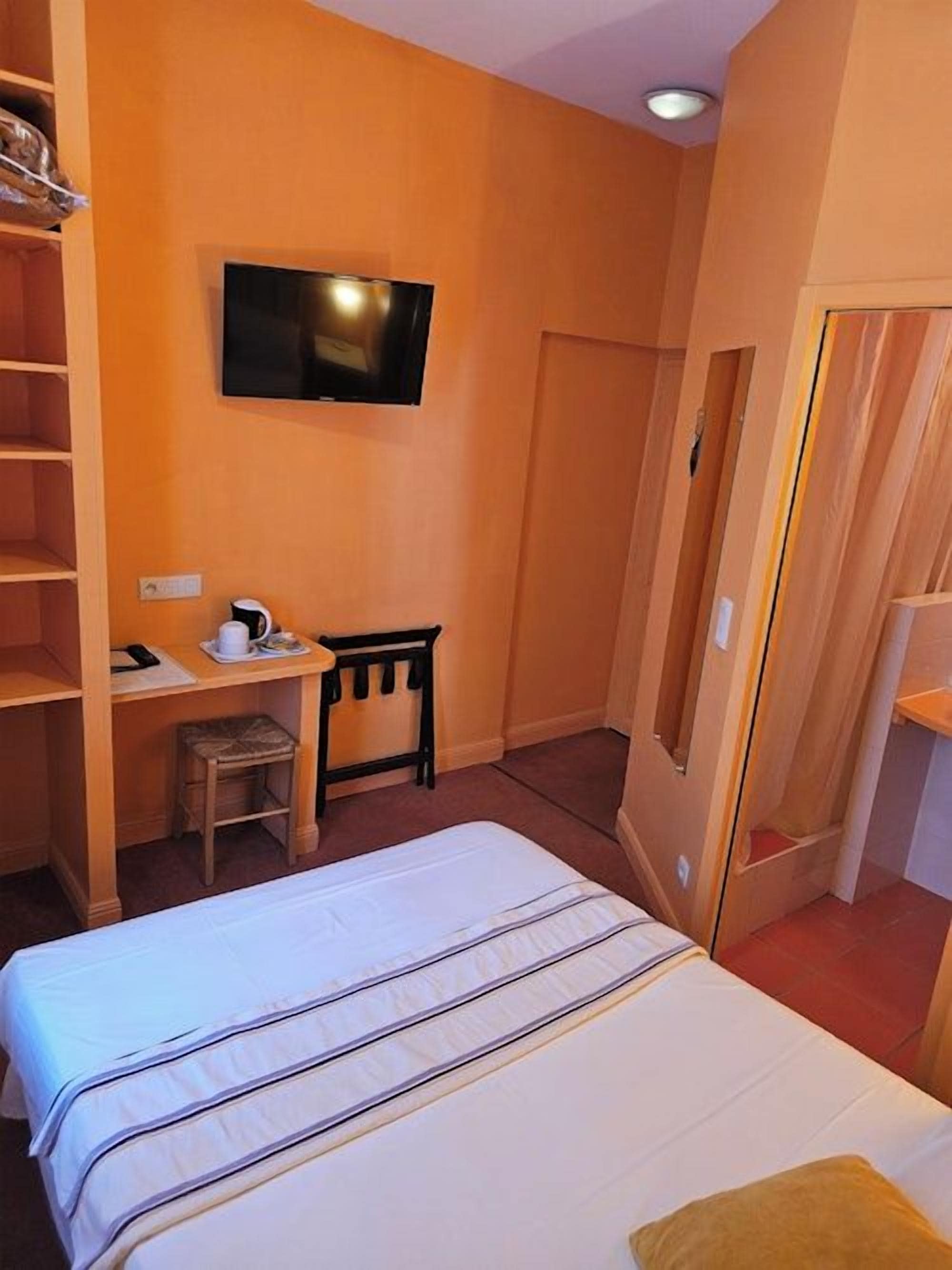 A hotel room with a bed, a desk with a chair, a television mounted on the wall, and a door.
