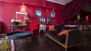 Une pièce avec un mur rouge, un canapé violet, un fauteuil rouge, une table ronde et un miroir.