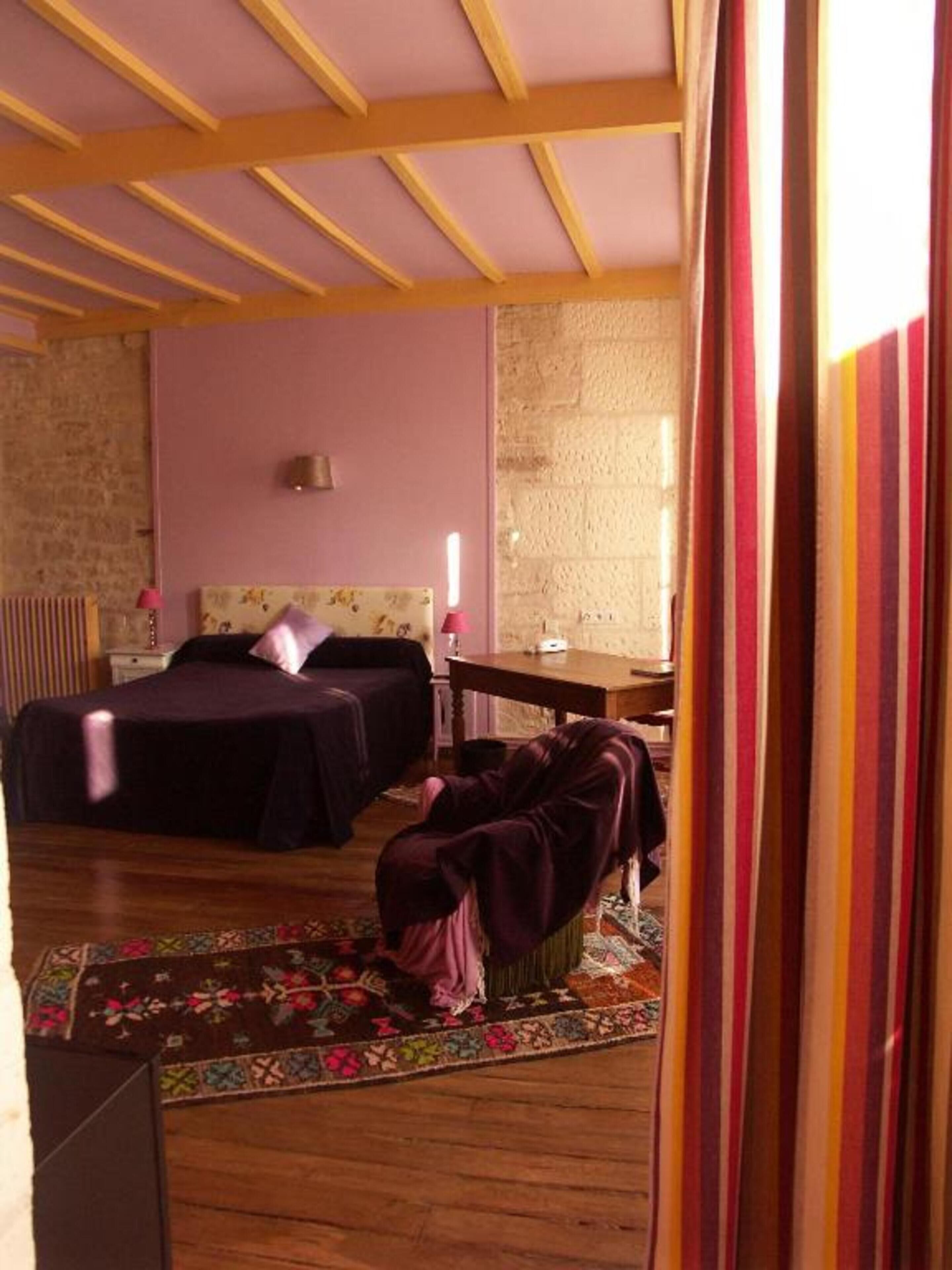 A bedroom with two beds, a wooden ceiling, a stone wall, and a small table.