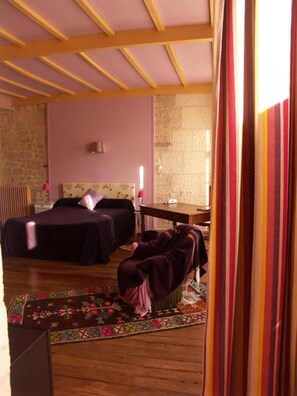 A bedroom with two beds, a wooden ceiling, a stone wall, and a small table.
