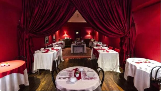 Un espace repas avec des rideaux rouges, des tables blanches et une table centrale sur laquelle est posé un gâteau.