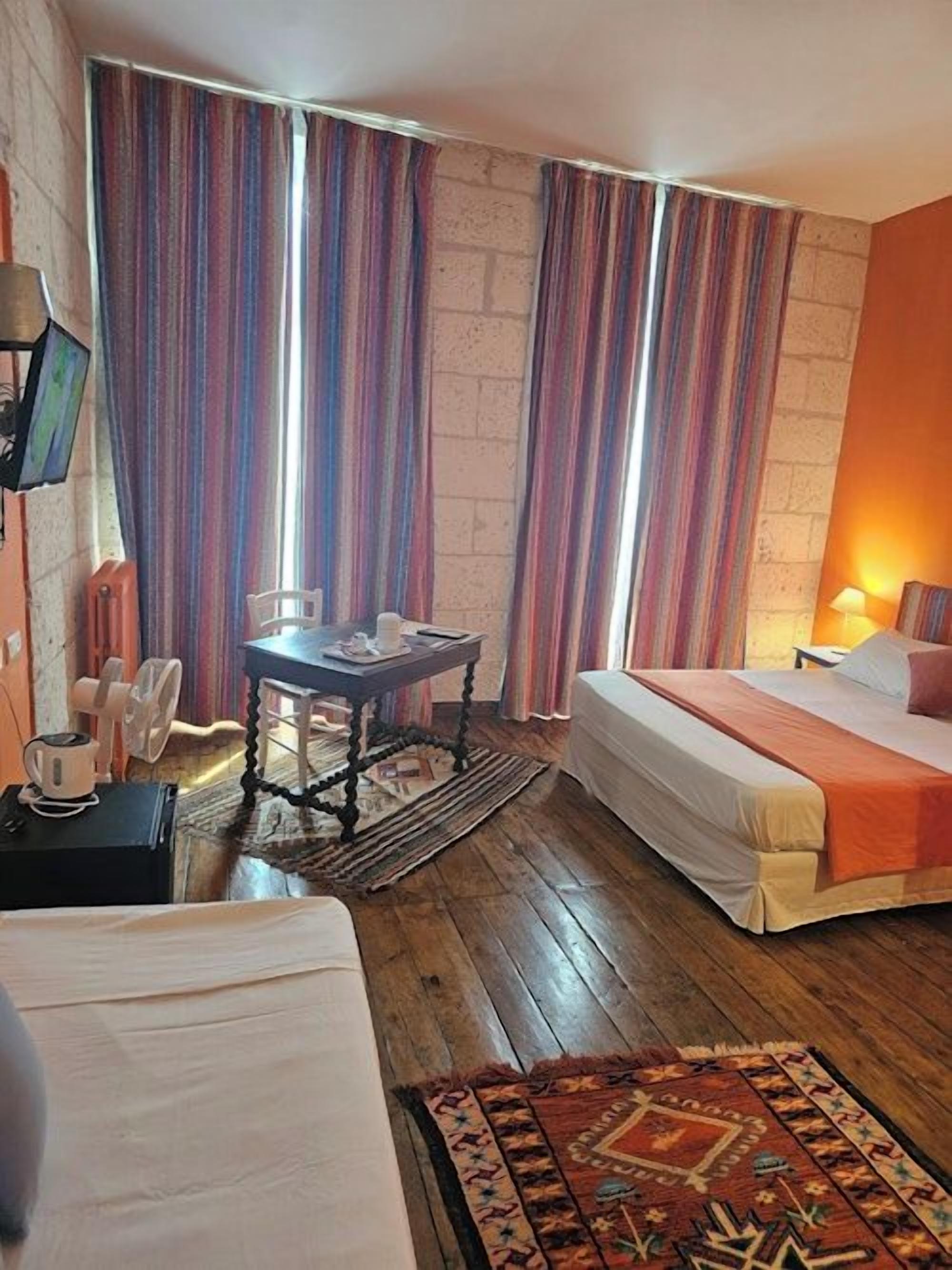 A hotel room with a bed, a small table, a chair, a TV, and a window with curtains.