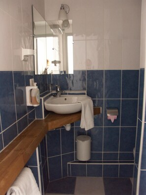 Un baño con un lavabo blanco, un espejo, una toalla colgada en la pared y un cubo de basura.