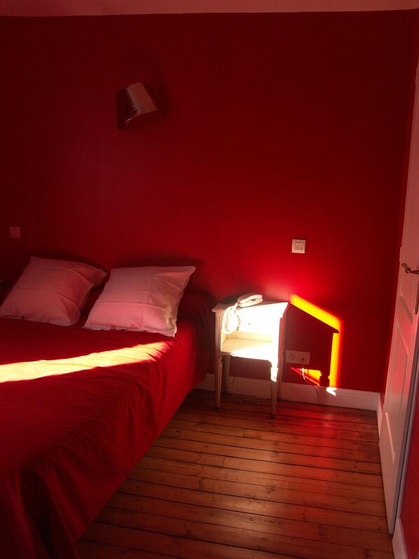 A room with a bed, a bedside table with a lamp, and a red wall.