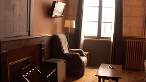 Une pièce avec une cheminée, un téléviseur fixé au mur, un canapé, une petite table et une fenêtre avec des rideaux.