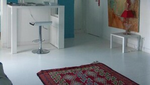Une pièce moderne avec un bureau blanc, deux chaises, une lampe rouge et un grand tableau abstrait accroché au mur.