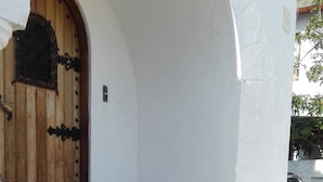 Entrada de un edificio con puerta de madera, plantas en macetas y un pequeño espacio de asientos al aire libre.