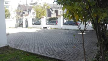 A paved courtyard with a small tree, a white wall, and a building with a tiled roof in the background.