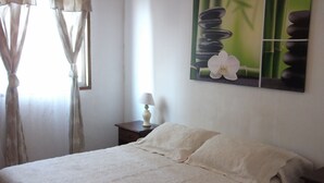 Un dormitorio con cama, mesita de noche, lámpara, ventana con cortinas y un cuadro en la pared.