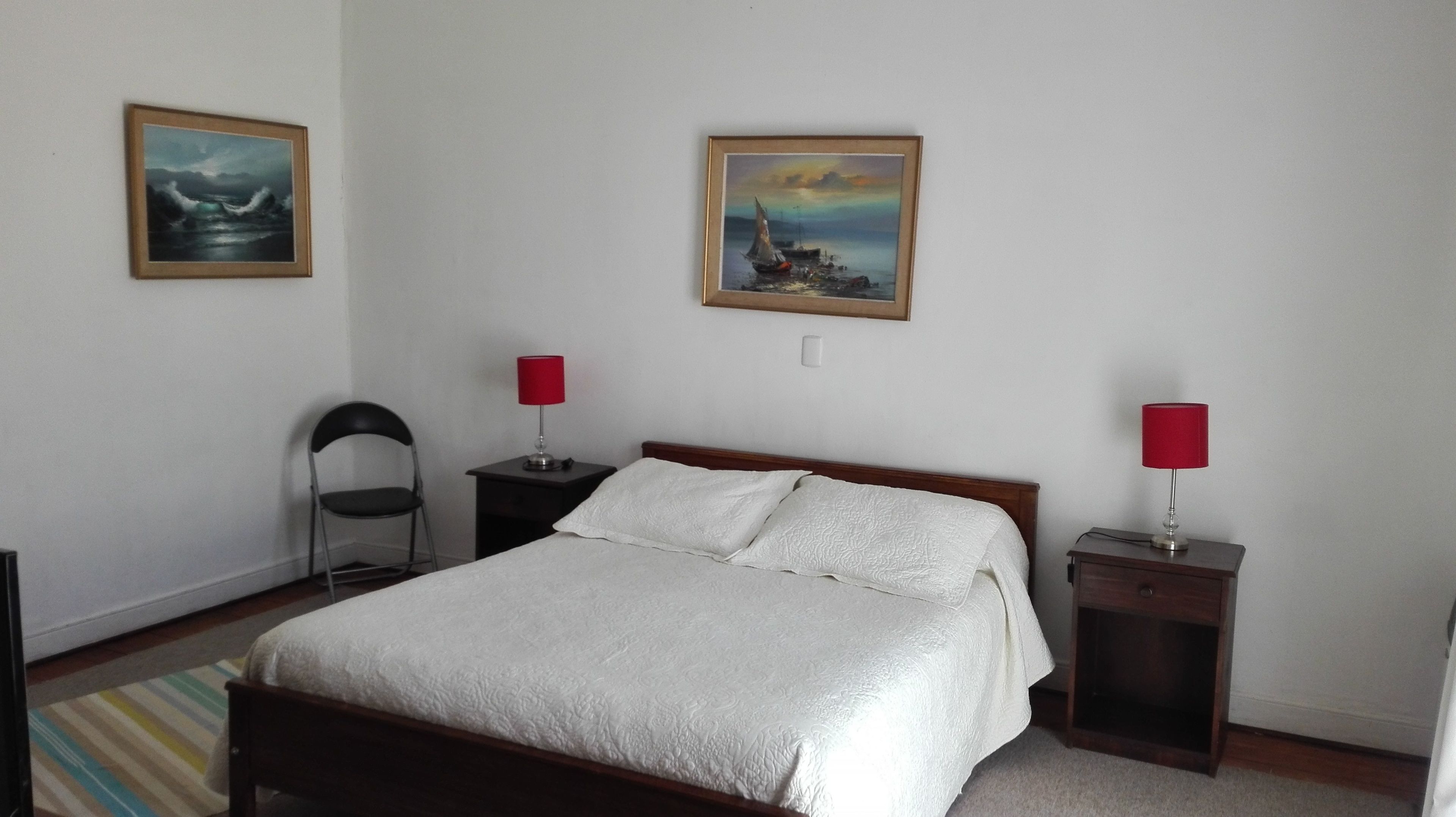 A bedroom with a bed, two nightstands, a chair, two paintings, and a striped rug.
