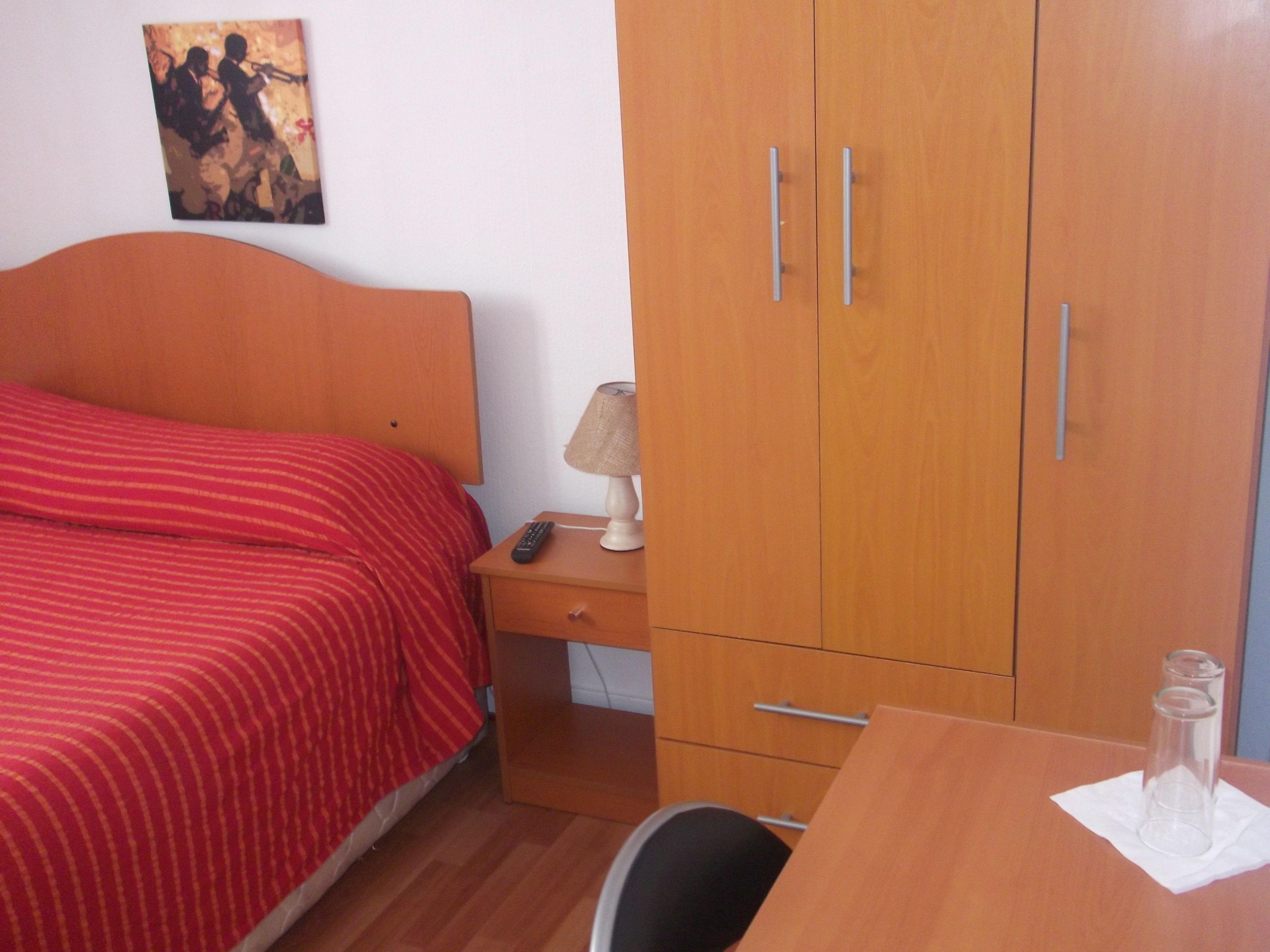 Une chambre à coucher comprenant un lit, une table de chevet, une lampe, une armoire et un bureau avec une chaise.