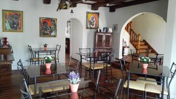 Un comedor con mesas y sillas de vidrio, una escalera de madera y dos cuadros en las paredes.