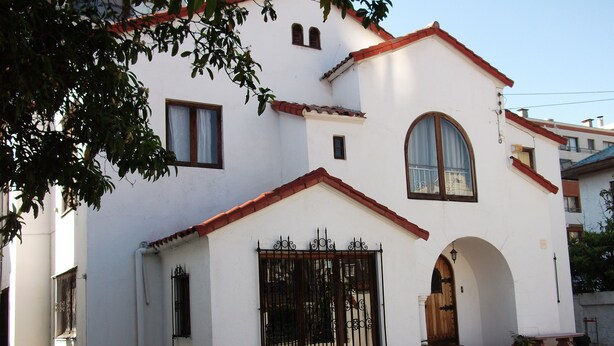 Un edificio blanco con techo de tejas rojas, un gran arco de entrada y una reja negra de hierro forjado.