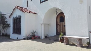 Un edificio con fachada blanca, techo de tejas, puerta de madera y un banco.