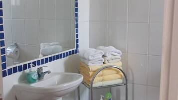 Un baño con lavamanos blanco, espejo y toallero con toallas dobladas.