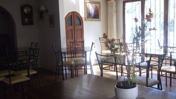 Un coin repas avec une table et des chaises en bois, une plante en pot et une porte visible au fond.